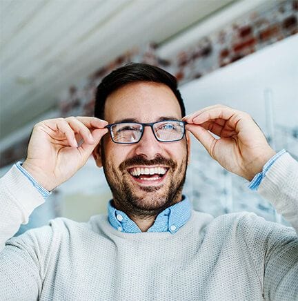 A smiling man adjusting his eyeglasses