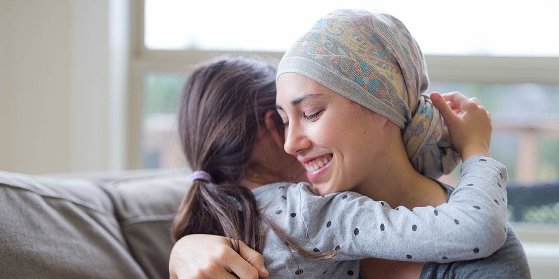A woman wearing a headscarf smiling as she hugs her daughter